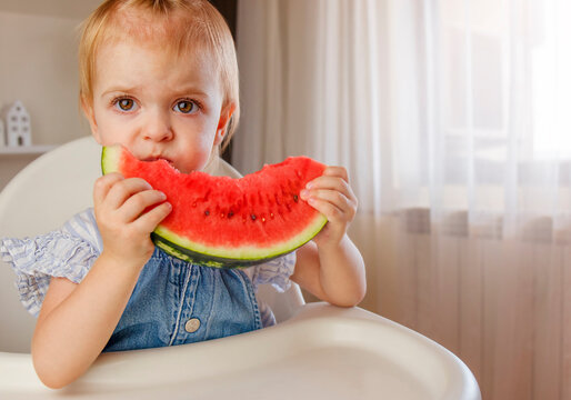 Little child with big red slice of watermelon sitting on highchair. Healthy eating concept. Healthy food at home