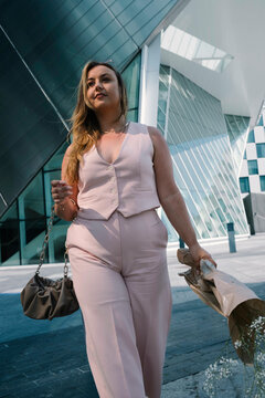 Sunny City Chic: Model Gleams in Pink Against Blue Windowed Structures