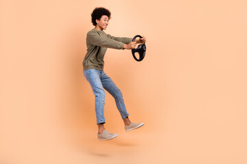 Full length photo of excited man professional driving simulation jump hold steering wheel fast speed auto school isolated on beige color background
