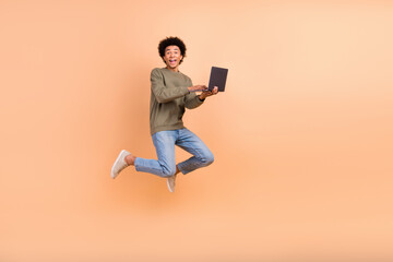 Full size portrait of crazy carefree person jump use wireless netbook empty space isolated on beige...