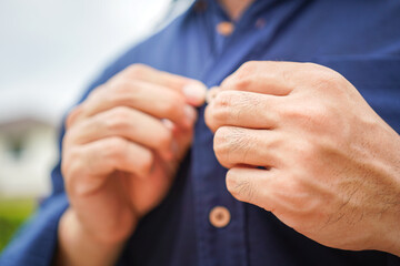 Action of a human hand is buttoning up the blue formal shirt, preparation for good clothing before going to work as the businessman concept. Close-up and selective focus on hand.