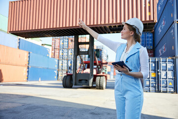 businesswoman holding tablet and wearing safety helmet in containers warehouse storage