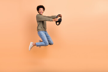 Fototapeta na wymiar Full body profile portrait of cheerful excited man jumping hold wheel empty space isolated on beige color background
