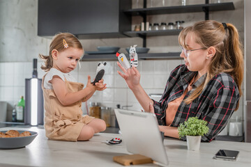 One young woman playing with toddler girl in the kitchen with finger puppets, babysitting at home...