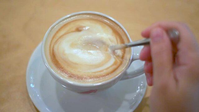 Womans hand stiring sugar with spoon in a cup of  cappuccino coffee. Top view. 