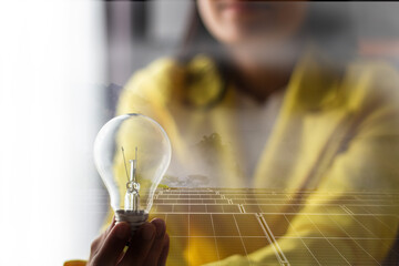 women in yellow suit holding light bulb on hand with solar cell screen in background 