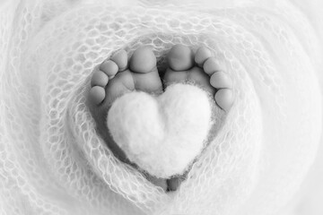Knitted heart in the legs of baby. The tiny foot of a newborn baby. Soft feet of a new born in a wool blanket. Close up of toes, heels and feet of a newborn. Macro photography. Black and white.