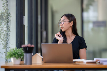 Freelance businesswoman wearing glasses uses laptop to search for information for project consideration, thinking work concept.