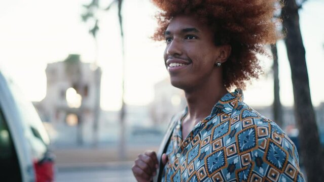 Smiling dark skinned male traveler walking at golden sunset light on street,enjoying summer vacation holidays and insured journey experience.Positive black man visiting touristic city for study abroad