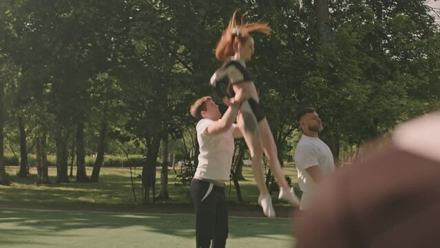 Slow motion shot of flyer girl performing cheerleading stunt with assistance of two base athletes during practice on outdoor soccer field