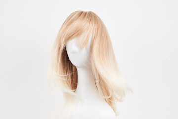 Naklejka premium Natural looking blonde wig on white mannequin head. Long hair on the plastic wig holder isolated on white background.