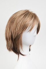 Natural looking dark brunet wig on white mannequin head. Short brown hair on the plastic wig holder isolated on white background.