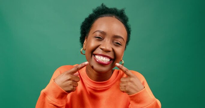 Beautiful young woman points to smile, white teeth, happy in green studio