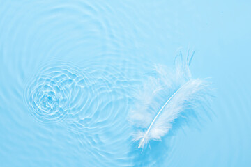 Water blue surface abstract background. Waves and ripples texture of cosmetic aqua moisturizer with bubbles and white feather.