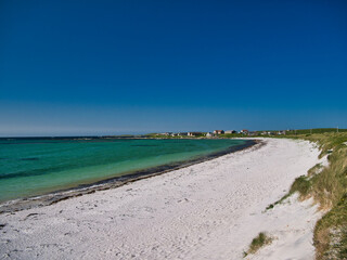 Obraz premium Bordered by the machair of the North Uist coast, the pristine beach of Traigh nam Faoghailean or Balranald Beach near Hougharry in the Outer Hebrides, Scotland, UK. Taken in sunshine with a blue sky.