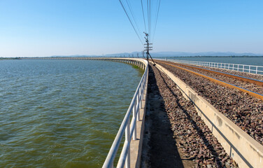 The curved concrete bridge of the railway line along the large reservoir.