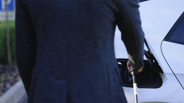 Close up of hand attaching power cable to environmentally friendly zero emission electric car. Businessman plugging electric car from charging station. Senior plugging in power cord to electric car