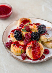Cheesecakes served in a ceramic plate, with raspberries and blackberries, sprinkled with honey and raspberry jam, sprinkled with powdered sugar.