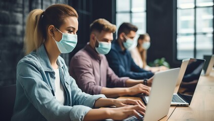 young businesspeople in medical masks working on laptops in office during covid-19 pandemic