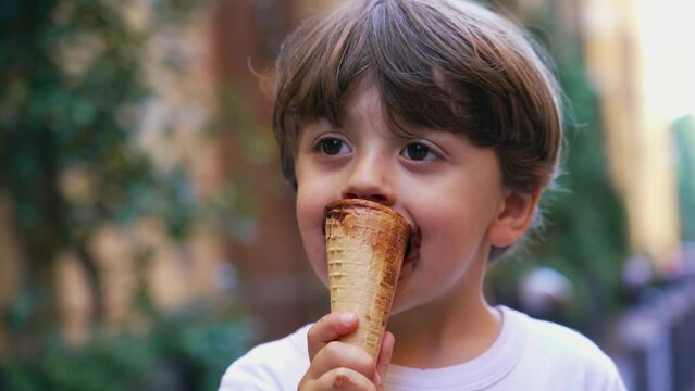 One cute little boy eating ice cream cone outside. Happy child eats ice cream food