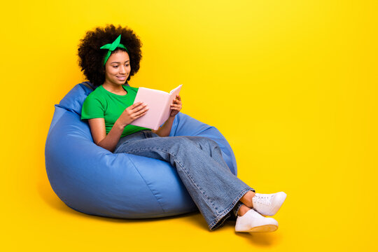 Full body portrait of cheerful teenager girl sit cozy bag read book empty space isolated on yellow color background