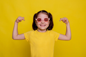 child girl points with finger on text on mockup yellow T-shirt on yellow background
