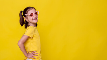 side view child girl posing on yellow background wearing sport T-shirt and retro pink sunglasses