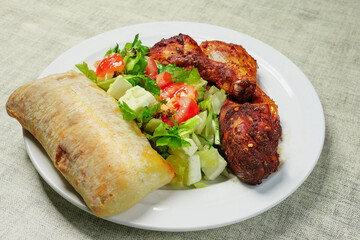 Cooked meal on a plate with marinated chicken drumsticks and fresh salad and Italian bread. Mediterranean style food. Selective focus. High quality product. Healthy eating.