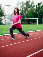 Fototapeta premium Young teenager girl doing stretching exercises on a running track. Selective focus. The model is slim body type. Light and airy look. Get ready for sport concept. Outdoor activity and lifestyle.