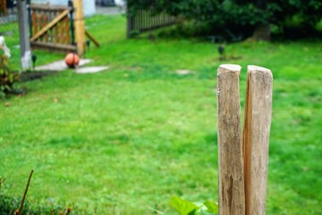 Garten Panorama mit braunem Holzzaunpfahl vor Wiese mit rotem Basketball vor offenem Holzzaun am Nachmittag im Sommer