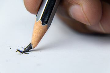 Fingers holding a pencil and nib broken while writing on white paper.