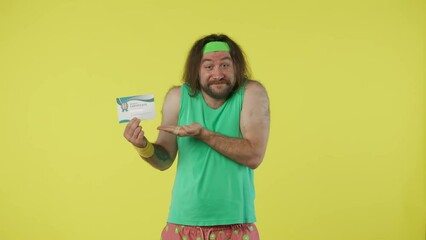 Man in green top and headband advertises sports gift certificate, smiling, pointing showing thumbs up. Isolated on yellow background.