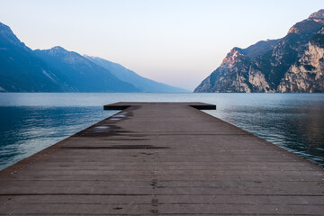 Wooden pier on the lake Garda against the backdrop of the mountains - obrazy, fototapety, plakaty