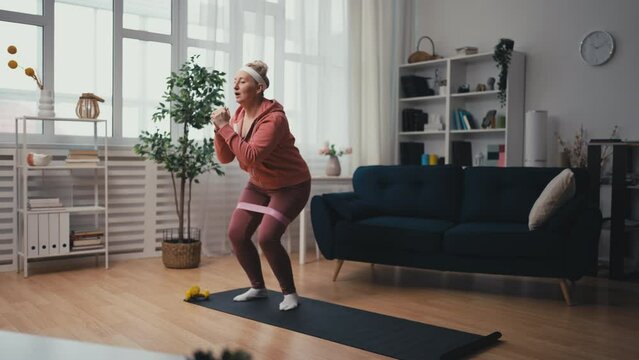 Middle-aged woman doing resistance band workout, exercising at home, fitness