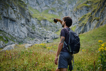 Man traveler with a backpack is taking a photo while hiking in the mountains. Traveling in nature. Rearview shot of a middle aged man hiking in the mountains. Bucegi Mountains,Romania