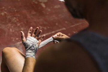 Crop unrecognizable boxing man sitting and wrapping hand with tape in daylight