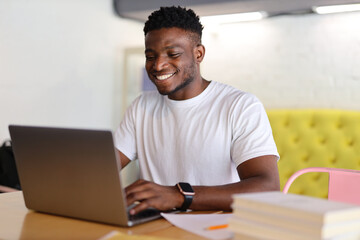 A young, cheerful African American businessman working happily on a laptop in a modern office.