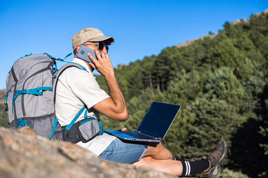 Mature traveler using mobil phone on rocky cliff