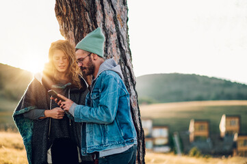 Couple of hikers using smartphone while walking along mountain grassy trail during a vacation