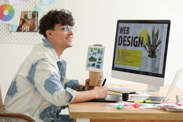 Male graphic designer with cup of coffee working at table in office - Powered by Adobe
