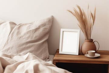 Portrait white frame mockup on retro wooden bedside table. Modern white ceramic vase, dry Lagurus ovatus grass. Cup of coffee and books in bed. Beige linen pillows in bedroom. Generative AI