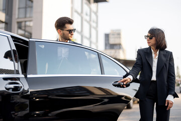 Female chauffeur helps a business man to get out of the car. opening a door. Concept of personal driver, luxury taxi or business trips