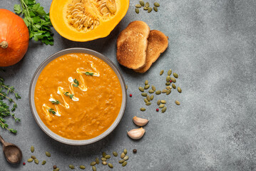 Pumpkin cream soup with toasts on a gray concrete background. Cozy thanksgiving dinner. Top view,...