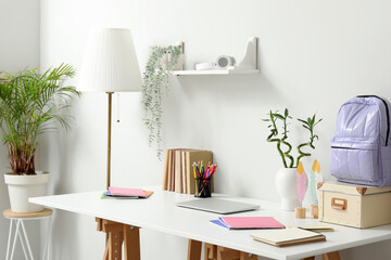 Modern school desk with laptop and stationery in room near white wall