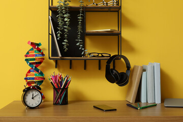 Modern school desk with molecular model, alarm clock and stationery in room near yellow wall