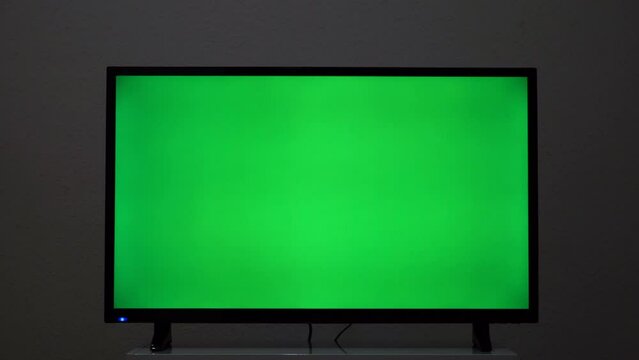 Close-up of TV screen with green background. Concept. Plasma TV screen with green screen. Modern TV on bedside table with green screen for insertion in house