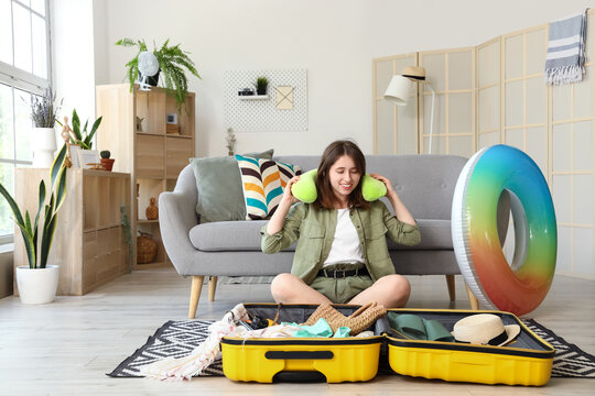 Young woman unpacking neck pillow from suitcase at home