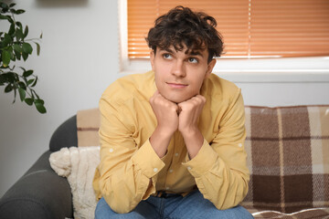 Portrait of thoughtful young man sitting on sofa in room