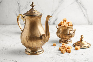 Vintage brass teapot and brown sugar cubes on white marble table