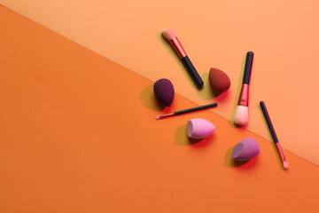 Makeup sponges and brushes on orange background